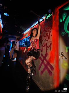 Person in gothic attire with fishnet stockings and platform boots in a neon-lit nightclub