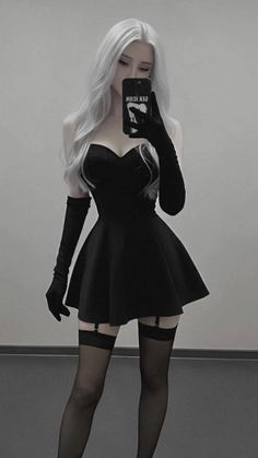 Woman with long white hair in a black dress and stockings taking a mirror selfie
