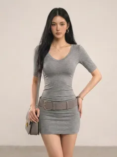 Woman in a gray dress with a belt and shoulder bag posing indoors