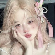 Woman with long pink hair and pink makeup, adorned with a ribbon and pearls