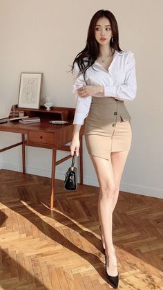 Woman in a white shirt and mini skirt holding a black handbag indoors