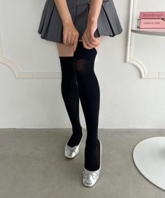 Person in a gray pleated skirt, black thigh-high socks, and silver shoes indoors