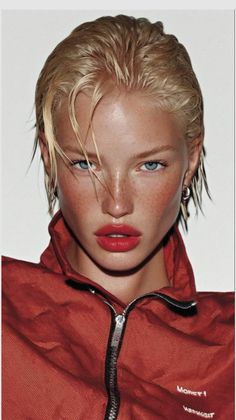 Blonde woman with wet hair, red lipstick, and freckles wearing a red jacket