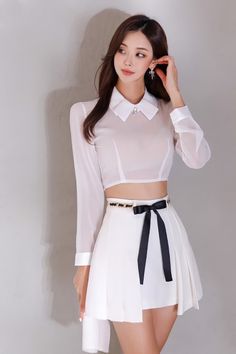 Woman in a white crop top and pleated skirt with a black ribbon