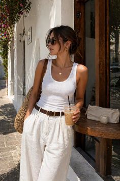 Woman in a white tank top and wide leg pants holding an iced coffee outdoors