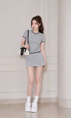 Woman in a gray skirt set with a ponytail and white sneakers indoors