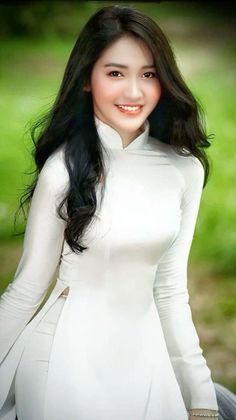 Woman with long black hair wearing a white ao dai and smiling outdoors