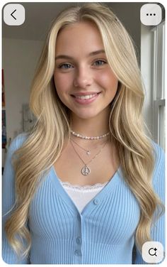 Smiling woman with blonde hair and blue eyes wearing a blue cardigan and layered necklaces