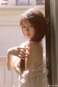Woman with long hair in a sheer white top, looking over her shoulder with soft backlight