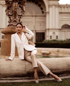 Woman in a white blazer and beige pants sitting on a fountain