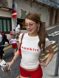 Woman in red shorts and white t-shirt holding a can on a street