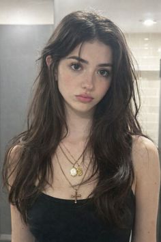 Young woman with long dark hair wearing a black tank top and layered necklaces