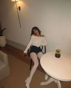 Woman in an off-shoulder top and white tights sitting indoors with a glass of wine
