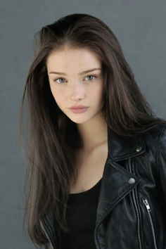 Woman with long dark hair wearing a black leather jacket and black top