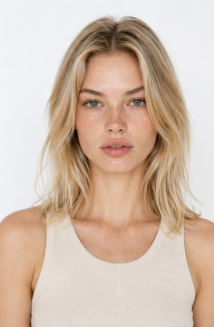 Woman with blonde hair and freckles wearing a tank top against a white background