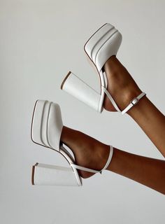 Two feet wearing white platform heels with ankle straps against a white background