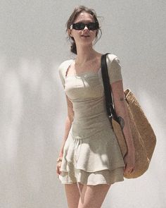 Woman in sunglasses and a ruffle skirt carrying a straw bag outdoors
