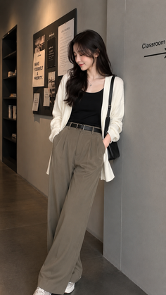 Woman with long dark hair wearing a white cardigan and wide leg pants indoors