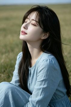 Woman with long black hair in a blue dress, eyes closed, enjoying the sun outdoors