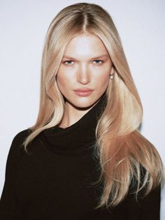 Woman with long blonde hair wearing a black turtleneck and pearl earrings