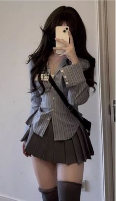 Person in a striped shirt and pleated skirt taking a mirror selfie
