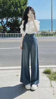 Woman in a white ruffled top and wide leg jeans taking a selfie outdoors