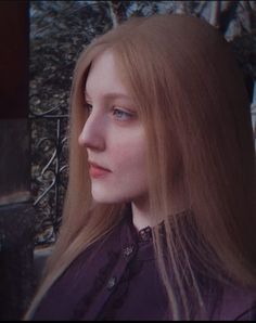 Woman with long blonde hair and blue eyes in a purple shirt with a lace collar