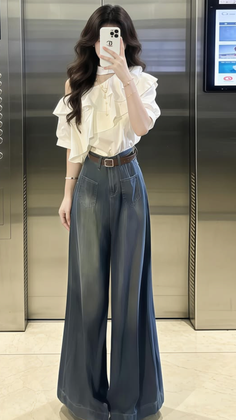 Woman in a white ruffle top and wide leg pants taking a mirror selfie