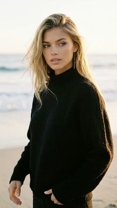 Woman with blonde hair in a black sweater on a beach at golden hour