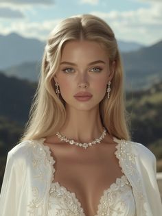 Blonde woman in a white dress and jewelry with mountains in the background