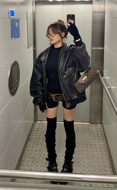 Woman in a black leather jacket and shorts taking a mirror selfie in an elevator