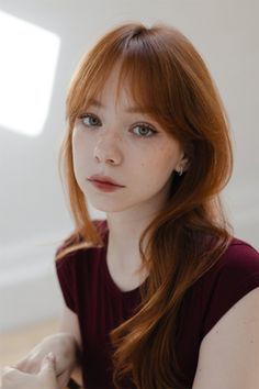 Young woman with red hair and freckles wearing a maroon shirt indoors