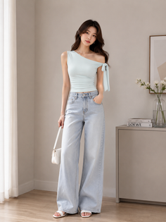 Woman in a light blue one-shoulder top and wide-leg jeans holding a white handbag