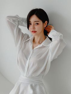 Woman in a white sheer shirt with arms raised, looking at the camera