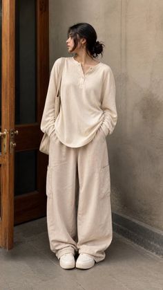 Woman in a long sleeve shirt and baggy pants standing indoors