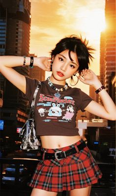 Woman in a plaid skirt and crop top posing against a sunset cityscape