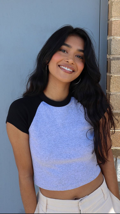 Woman with long dark hair wearing a crop top and hoop earrings, smiling outdoors