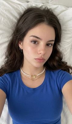 Young woman with long brown hair wearing a blue t-shirt and pearl necklace