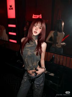 Woman in a camo top and jeans with exposed skin in a dark indoor setting