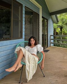 Woman with dark hair in a white blouse and floral skirt sitting on a porch