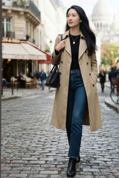 Woman in a trench coat and jeans walking on a cobblestone street