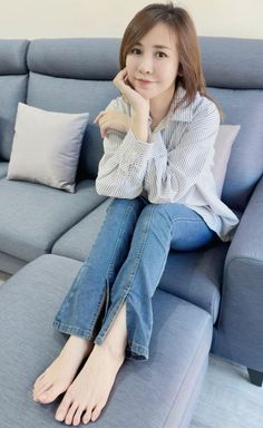 Woman with long hair in a striped shirt and blue jeans sitting on a sofa