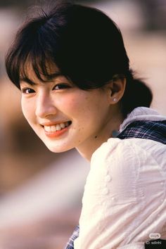 Smiling woman with black hair and freckles wearing a white and plaid shirt