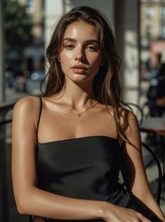 Woman with long hair wearing a black dress and necklace, bathed in soft sunlight