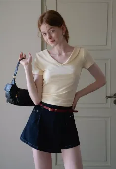 Woman with red hair wearing a yellow top and denim shorts, holding a black handbag