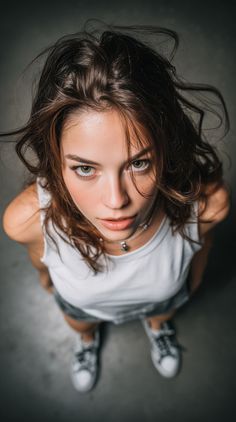 Woman with long hair and a white tank top looking up at the camera