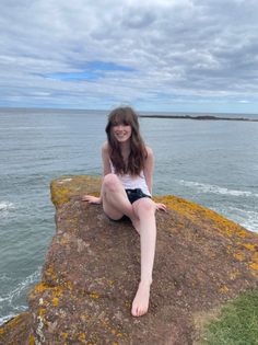 Young woman with long hair sitting on a rocky cliff overlooking the ocean