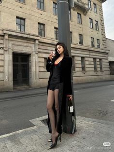 Woman in a long black coat and shorts holding a champagne glass and wine bottle on a street