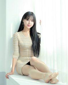 Woman with long black hair in a striped dress sitting by a window