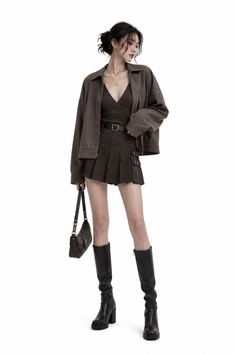 Woman in a brown jacket and pleated skirt with knee-high boots and a handbag